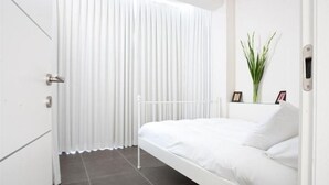 A bedroom with a white bed, a white wardrobe, and a window with vertical blinds.