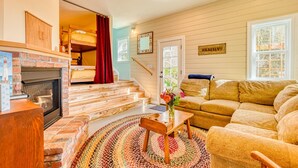 Ein gemütliches Wohnzimmer mit Kamin, einer Sofagarnitur, einem kleinen Tisch mit einer Vase und einer Treppe, die in einen anderen Raum führt.