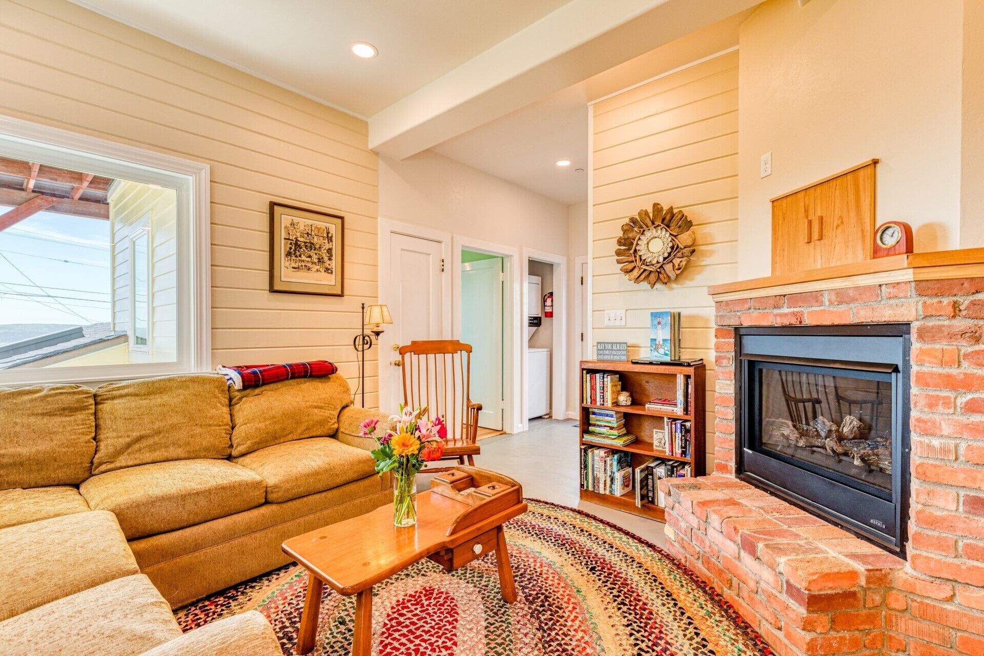 A cozy living room with a sofa, a coffee table with a vase of flowers, a fireplace, and a bookshelf.
