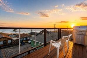 Terraza de madera con una parrilla y sillas con vista a una playa y al océano.