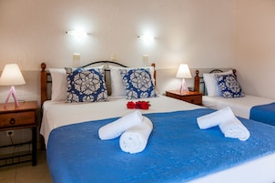Habitación de hotel con dos camas, cada una con cubrecama azul y ropa de cama blanca, dos mesitas de noche con lámparas y un cabecero estampado con motivos florales.