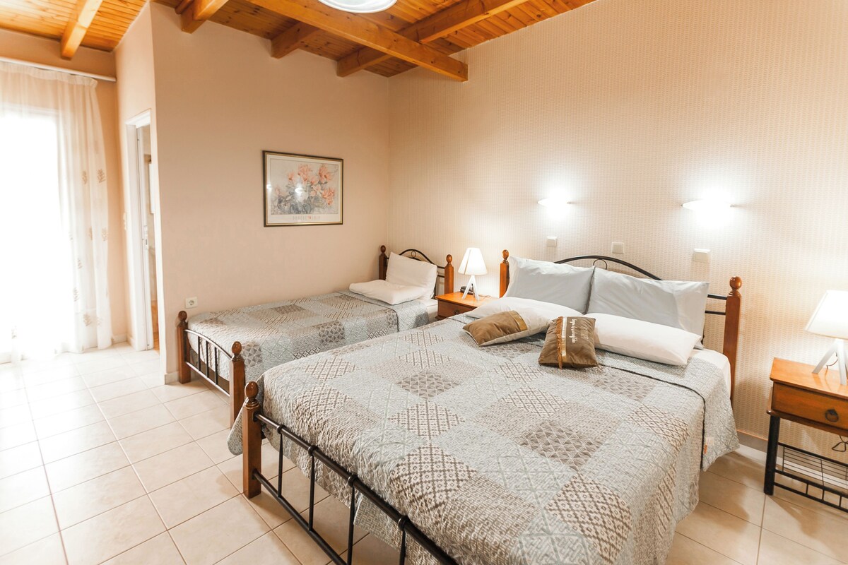 A hotel room with two beds, a wooden ceiling, a painting on the wall, and a nightstand with a lamp.