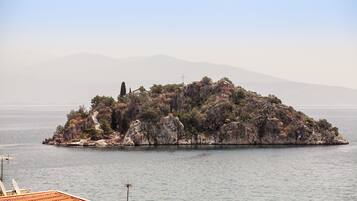 A small rocky island with a cross on top, surrounded by calm water and distant mountains.