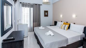 A hotel room with a bed, a desk, a chair, a window with curtains, an air conditioning unit, and a wall-mounted picture.