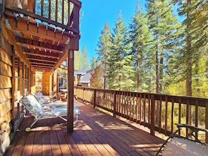 Eine Holzterrasse mit überdachter Sitzecke und Blick auf einen Wald.