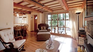 Un salón acogedor con vigas de madera, un comedor y un amplio ventanal con cortinas.