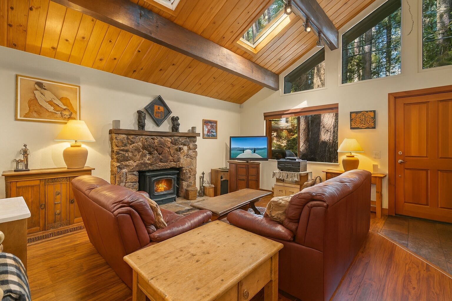 A cozy living room with a stone fireplace, leather sofas, a wooden coffee table, and a television.