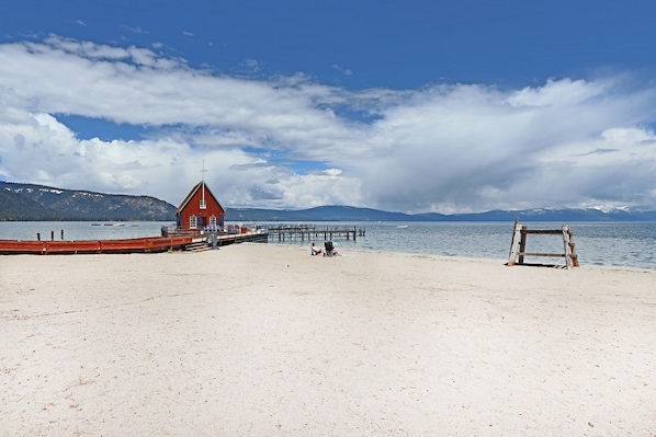 Une plage avec un bâtiment rouge, une structure en bois et une jetée qui s’avance dans l’eau.