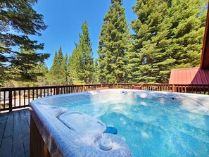 Un bain à remous entouré d’une terrasse en bois, offrant une vue sur de grands arbres et un ciel bleu dégagé.