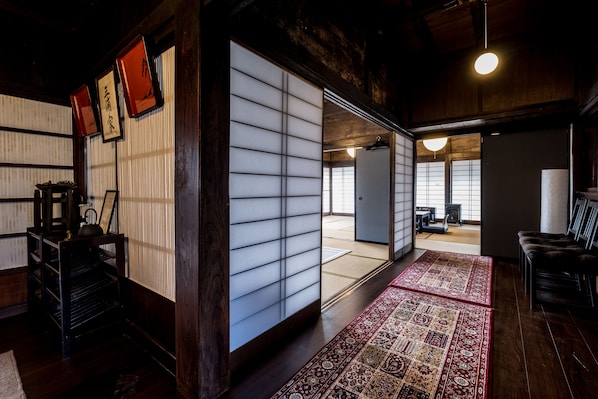 A traditional Japanese room with tatami flooring, shoji screens, and a red patterned rug.