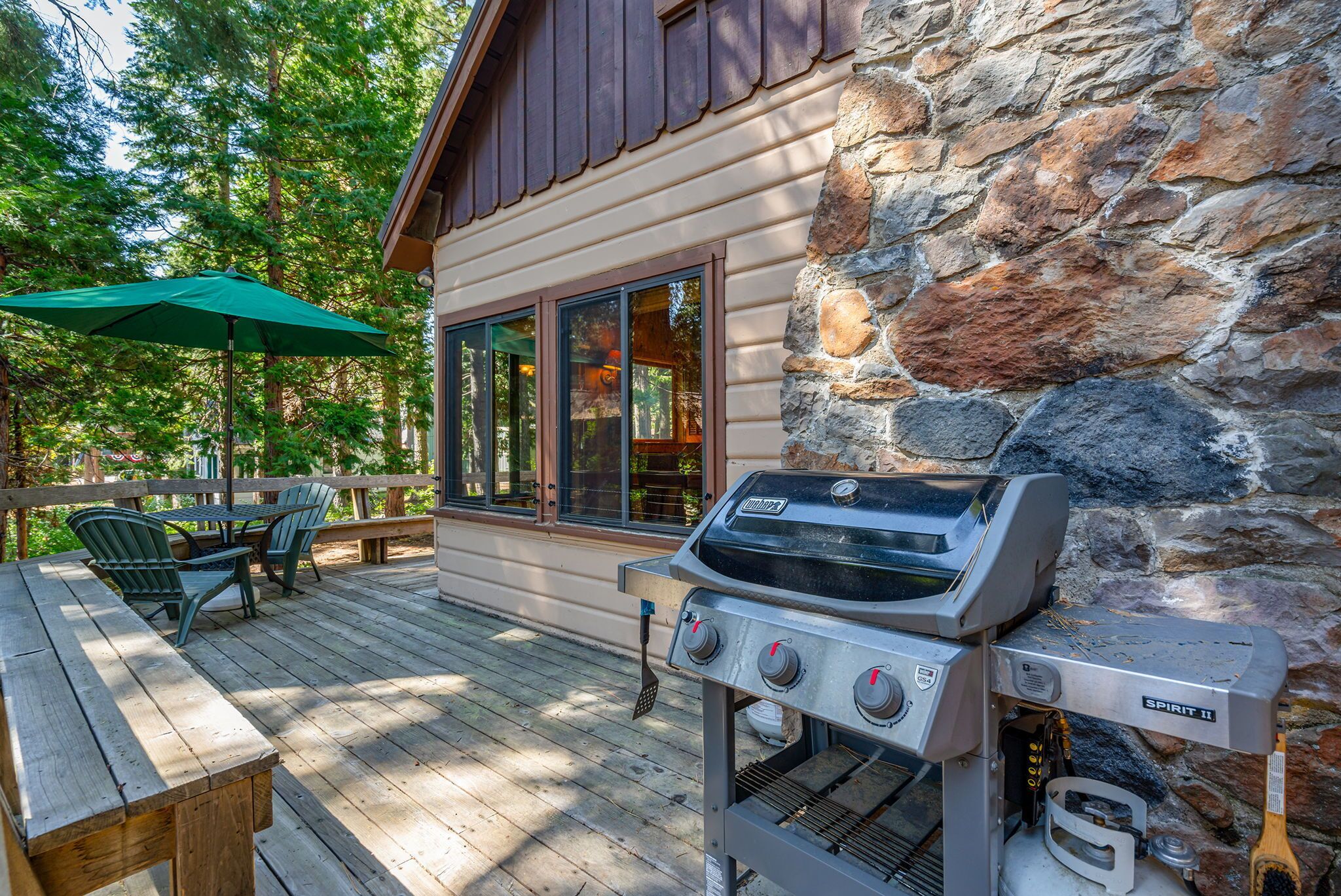 A wooden deck with a grill, outdoor furniture, and a stone wall.