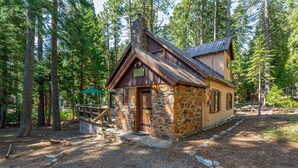 A rustic cabin with a stone exterior and wooden trim, surrounded by tall pine trees. - Quandt Cabin - Old Tahoe Cabin - WALK TO LAKE! (Tahoe City)