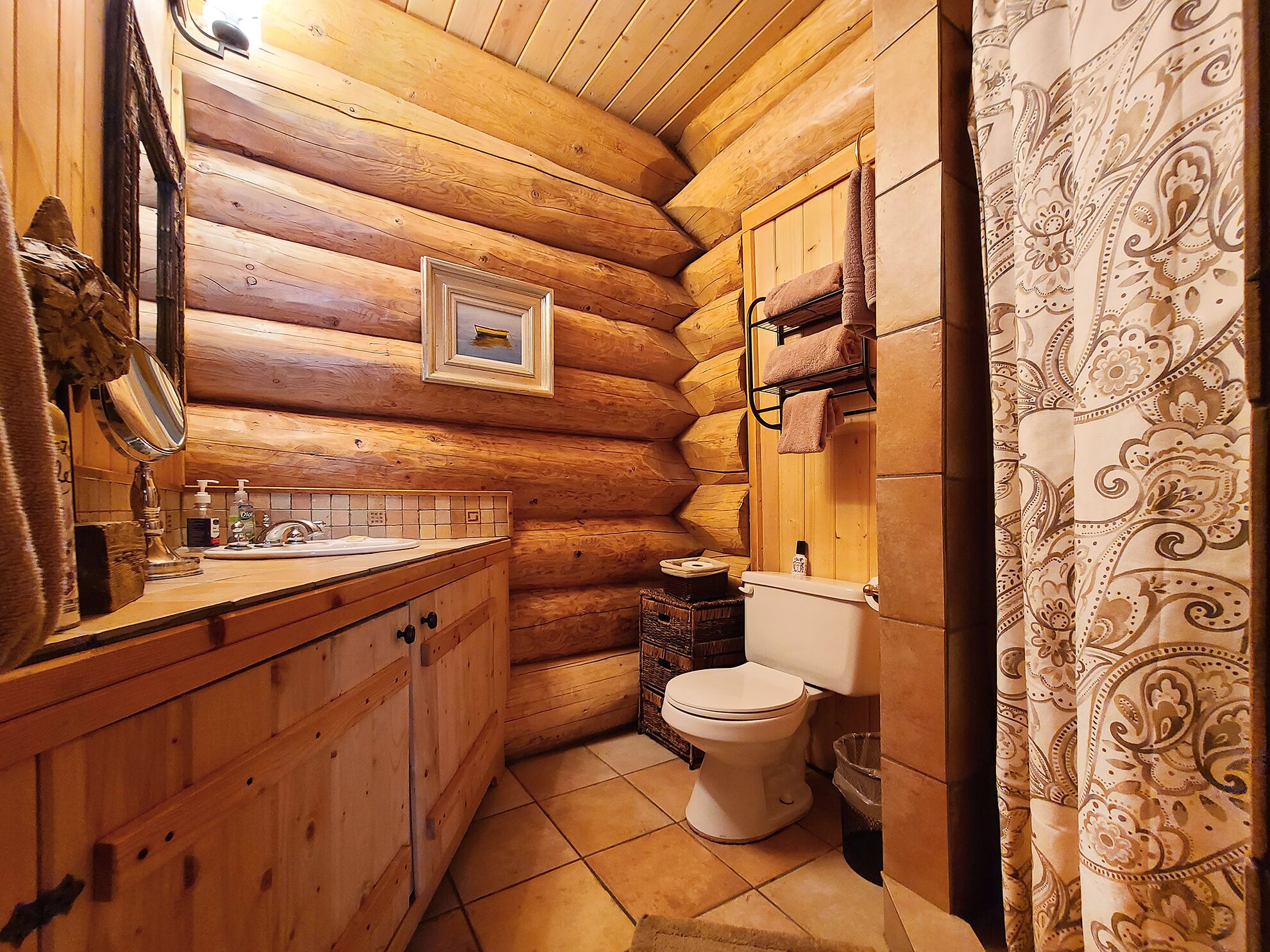 Une salle de bain rustique, avec des murs en bois, un lavabo en bois, des toilettes et un miroir.