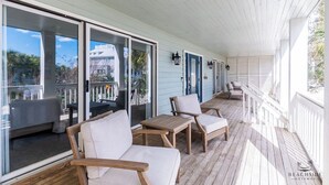 Een overdekt terras met houten meubels, glazen deuren en uitzicht op de oceaan.