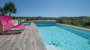 Una piscina con sillones de descanso y un jacuzzi en una terraza de madera.