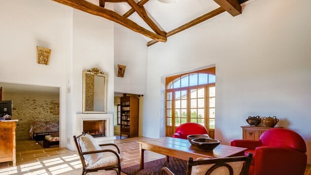 Un salón amplio con chimenea, sillas rojas, una mesa de madera y un ventanal grande.