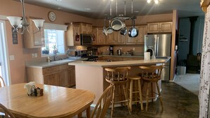 A spacious kitchen with wooden cabinets, a large island with bar stools, and modern appliances. - Peace and privacy await among the towering Pine Trees. (Bayfield)