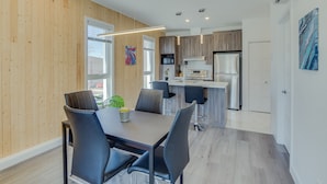 Une cuisine moderne dotée de meubles en bois, d’appareils électroménagers en acier inoxydable et d’un coin repas avec une table et des chaises.