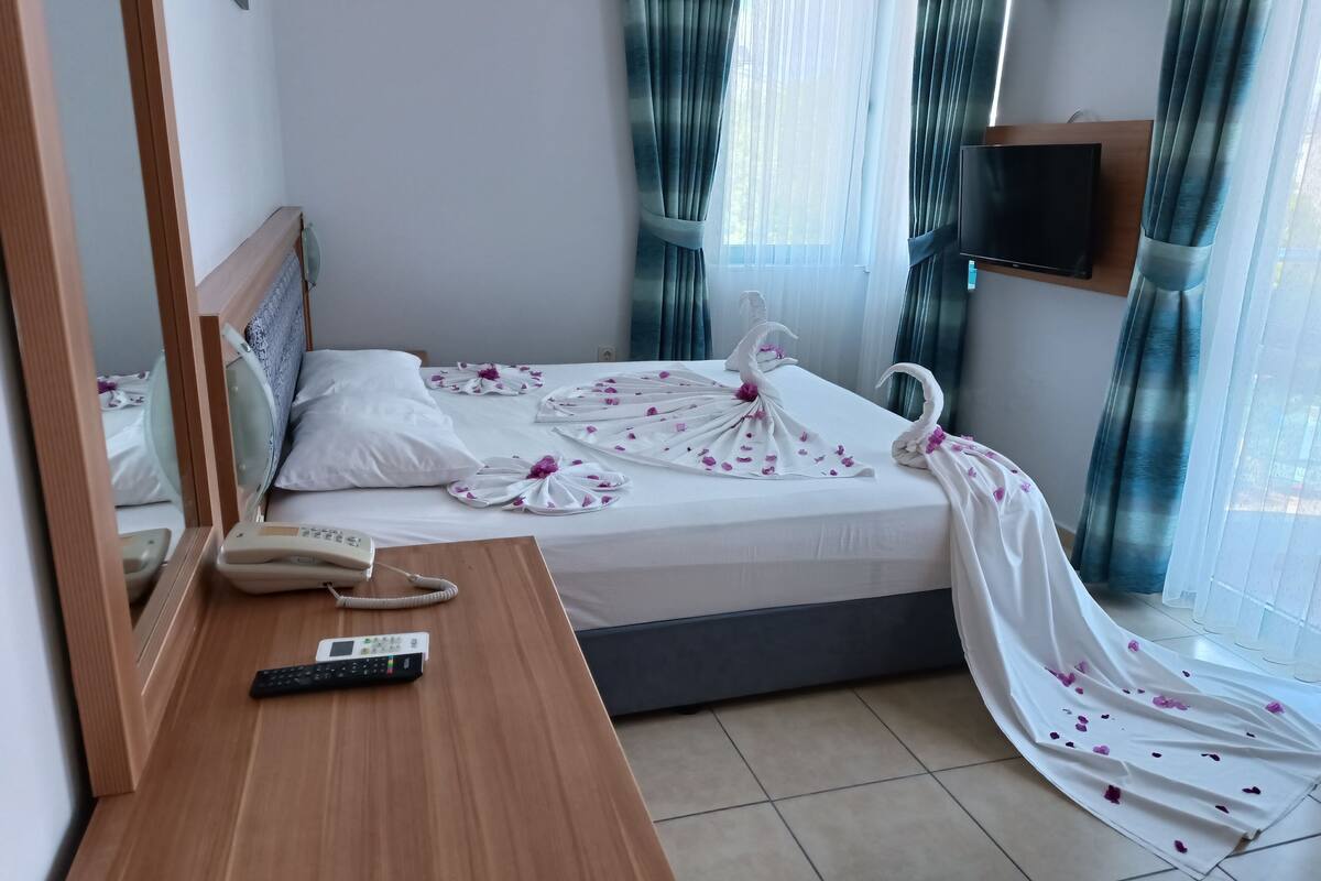 Ein Hotelzimmer mit einem Bett, einem Nachttisch mit Telefon und Fernbedienung, einem Spiegel und einem an der Wand befestigten Fernseher.