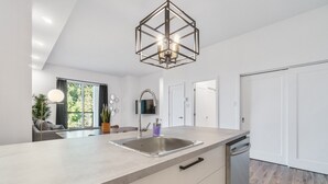 Une cuisine moderne dotée d’un grand îlot central, d’un évier en acier inoxydable et d’un luminaire suspendu au design géométrique.