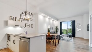 Une cuisine moderne dotée d’un lave-vaisselle encastré, un coin repas avec une table et des chaises, et une grande fenêtre offrant une vue sur la verdure.