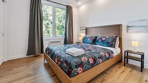 Une chambre à coucher avec un lit en bois, une literie à motifs floraux, une table de chevet avec une lampe et une fenêtre avec des rideaux.