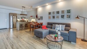 Una sala moderna con un sofá gris, un comedor con sillas de madera, una cocina con refrigerador de acero inoxidable y obras de arte con temática urbana.