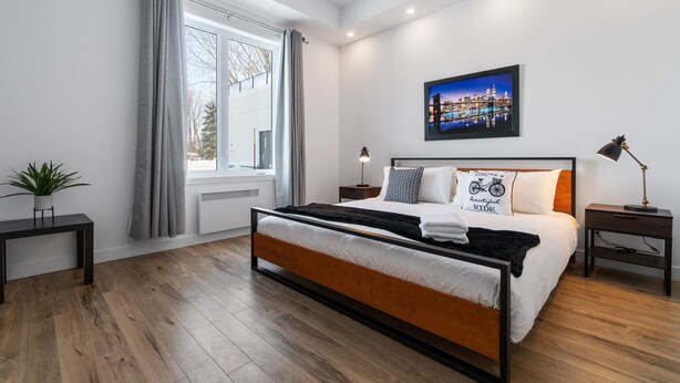 Un dormitorio moderno con una cama grande, un cuadro de un paisaje urbano y una ventana con cortinas.