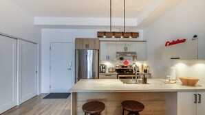 Una cocina moderna con una isla central, electrodomésticos de acero inoxidable y taburetes de bar de madera.