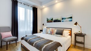 Een netjes ingerichte slaapkamer met een bed, een stoel, een nachtkastje en een lamp.