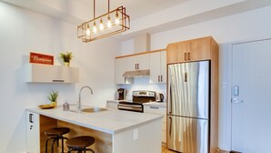 A modern kitchen with a central island, stainless steel appliances, and a wooden cabinet. - L'île-Do | condos neufs sur l'ile d'Orléans, The Bouquet - 801 (Saint-Pierre-de-l'Île-d'Orléans)