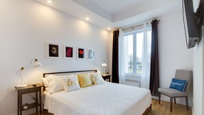A neatly arranged bedroom with a bed, bedside tables, a chair, and a window with curtains. - L'île-Do | condos neufs sur l'ile d'Orléans, The Bouquet - 801 (Saint-Pierre-de-l'Île-d'Orléans)