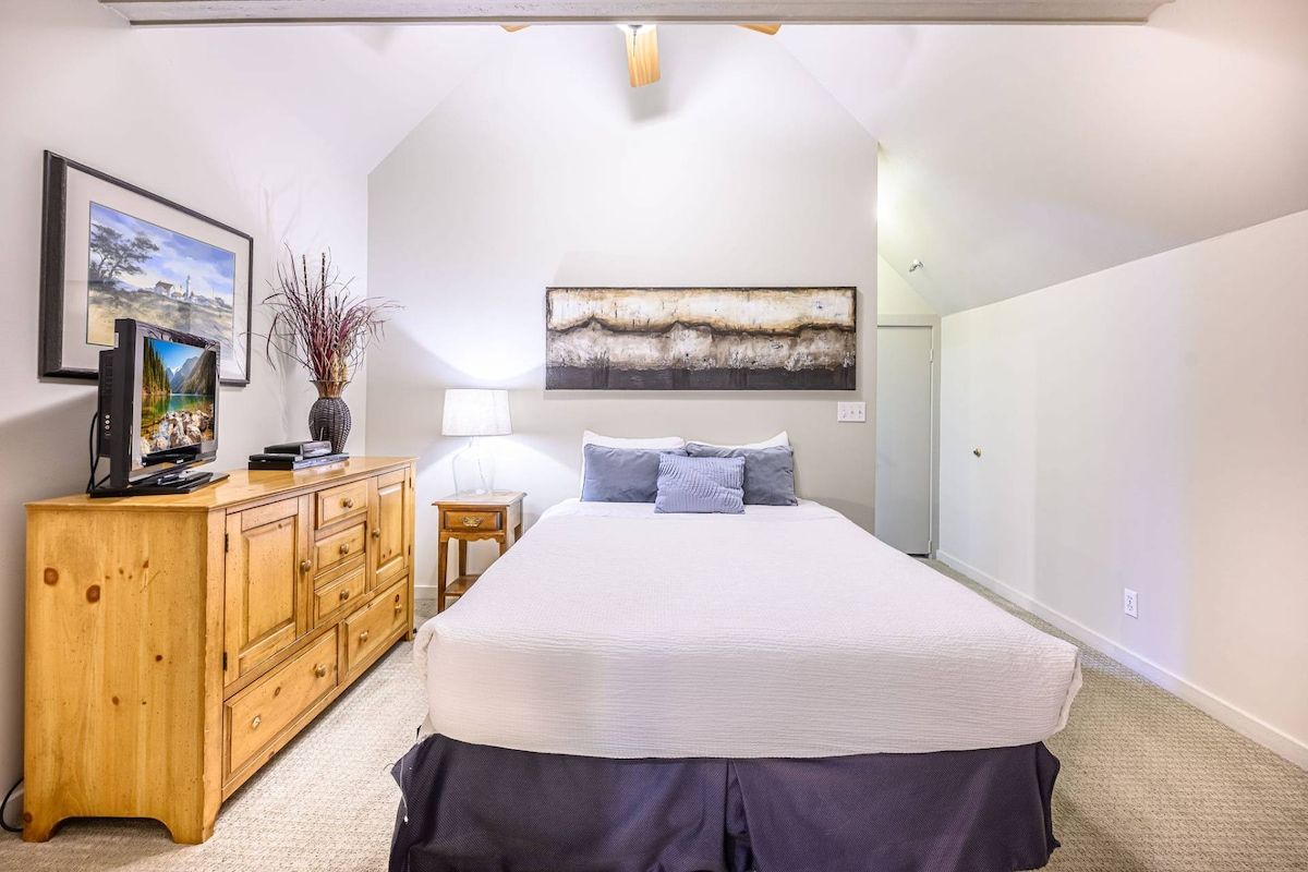 A bedroom with a bed, a wooden dresser, a television, and artwork on the walls.