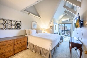 Quarto com cama, penteadeira de madeira, escrivaninha e cadeira. Há uma janela com vista para o exterior.
