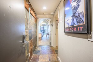 A hallway with a tiled floor, a door on the left, and a poster on the right.