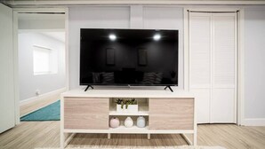 Una sala de estar moderna con un televisor de pantalla plana sobre un mueble blanco, una planta pequeña y tres jarrones.
