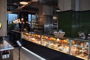 Eine Feinkosttheke mit einer Auswahl an Käse, Fleisch und Gemüse. Hängende Lampen und ein Menüständer sind vorhanden.