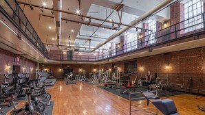 Uma academia ampla com equipamentos de ginástica, piso de madeira e um mezanino.