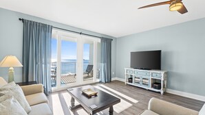 A living room with a sofa, coffee table, TV, and a balcony with curtains.
