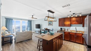 A spacious living area with a sofa, a dining table, and a kitchen with wooden cabinets and a refrigerator.