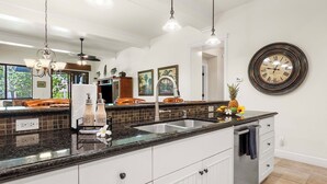 Een moderne keuken met een groot schiereiland, roestvrijstalen apparatuur en een decoratieve klok aan de muur.
