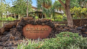 Een bord voor KULALANI bij Mauna Lani, met een natuurlijke rotsformatie en tropische begroeiing op de achtergrond.