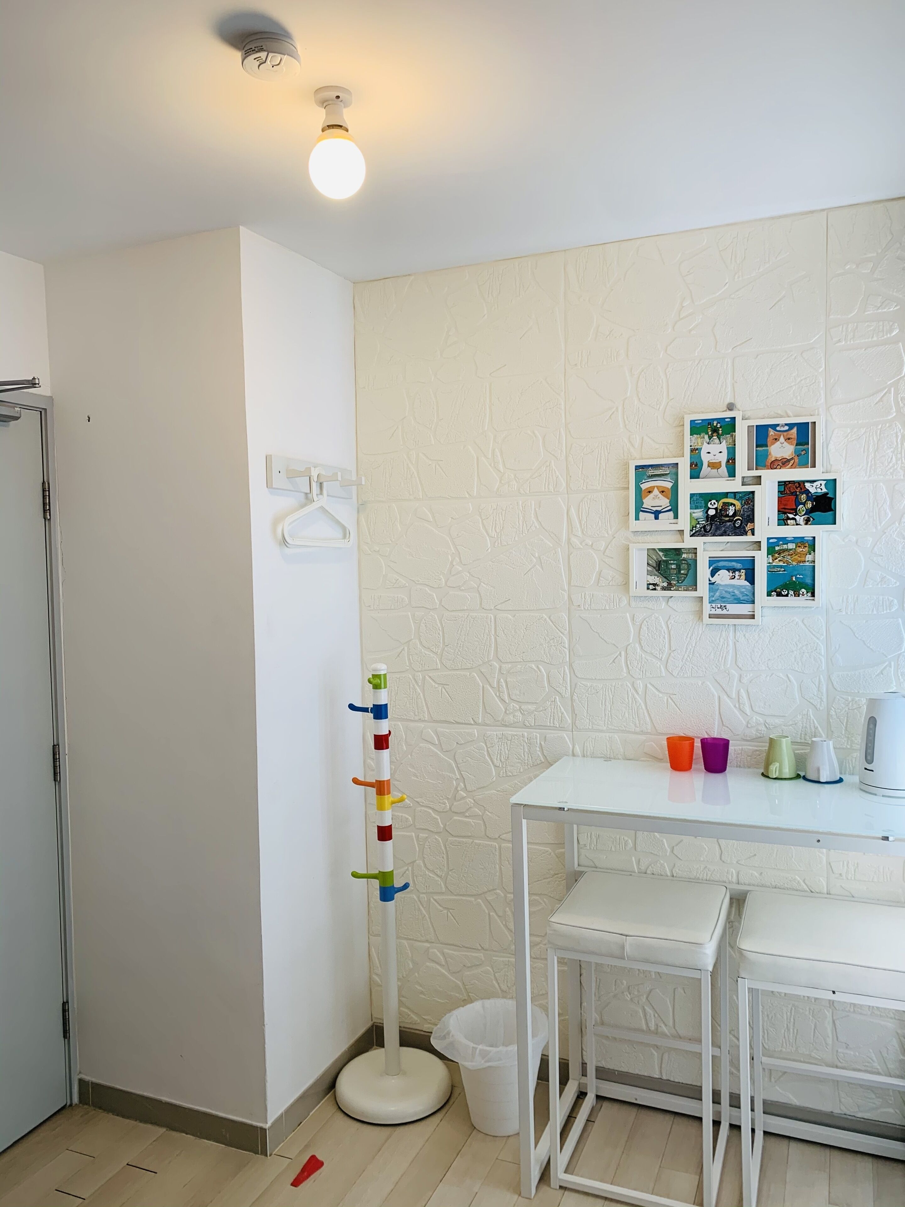 Een kleine, schone kamer met een witte muur, een witte tafel en een prikbord met kleurrijke spullen.