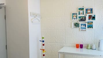Een kleine, schone kamer met een witte muur, een witte tafel en een prikbord met kleurrijke spullen.