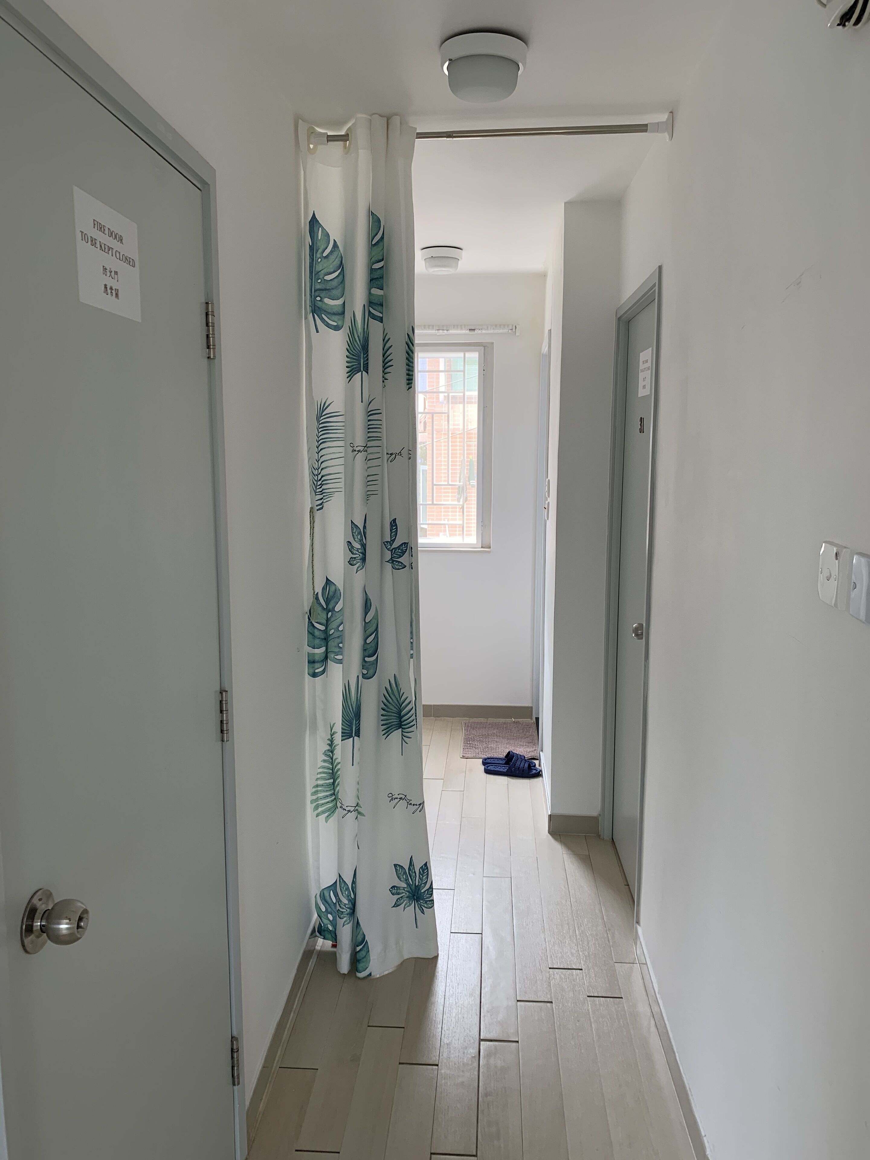 A hallway with a fire door, a window with a view, and a door with a sign.