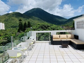 Une terrasse avec des sièges extérieurs, une vue sur une montagne et un bâtiment en arrière-plan.