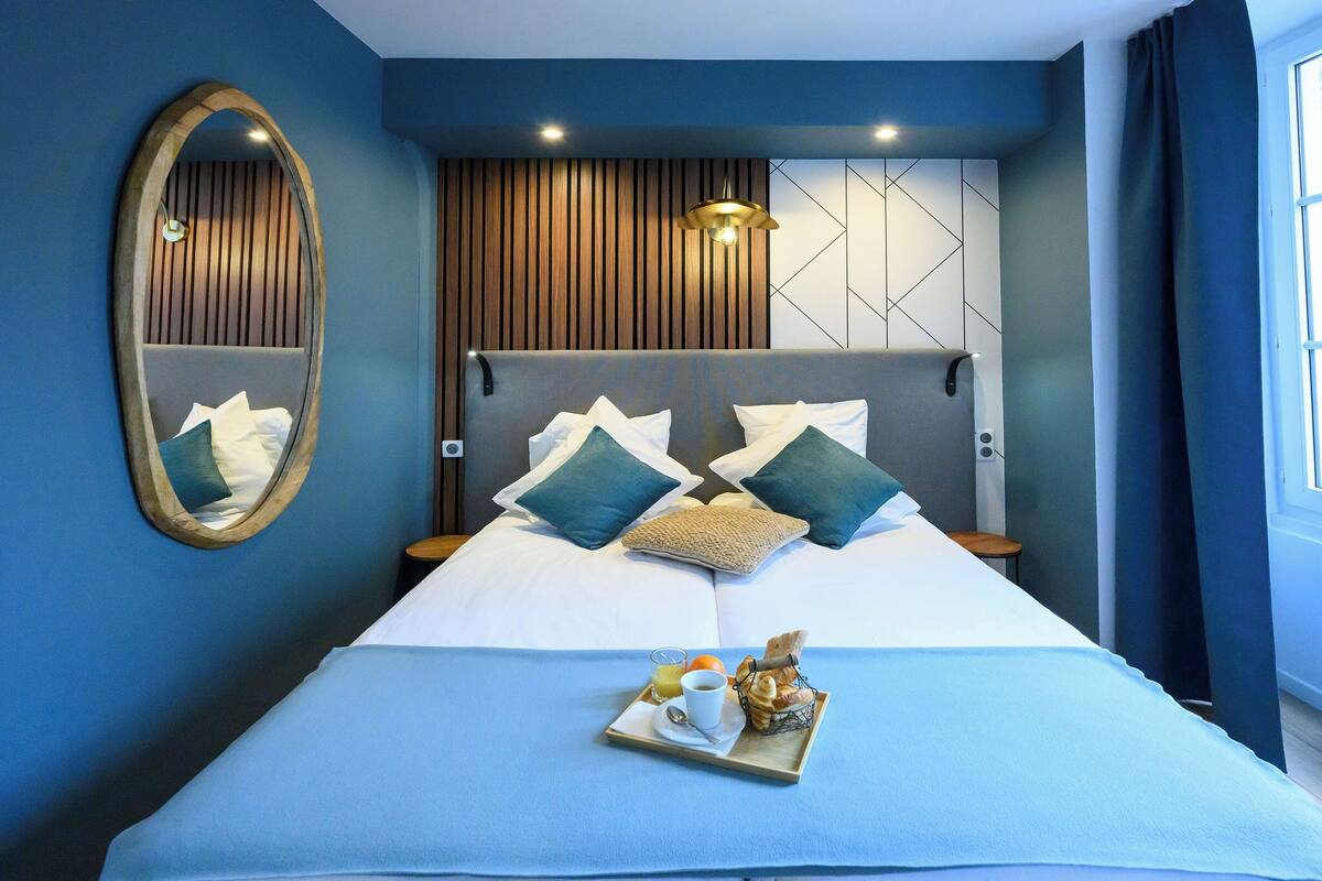 A modern hotel room with a large bed, a wooden headboard, a tray with breakfast items, and a mirror on the wall.
