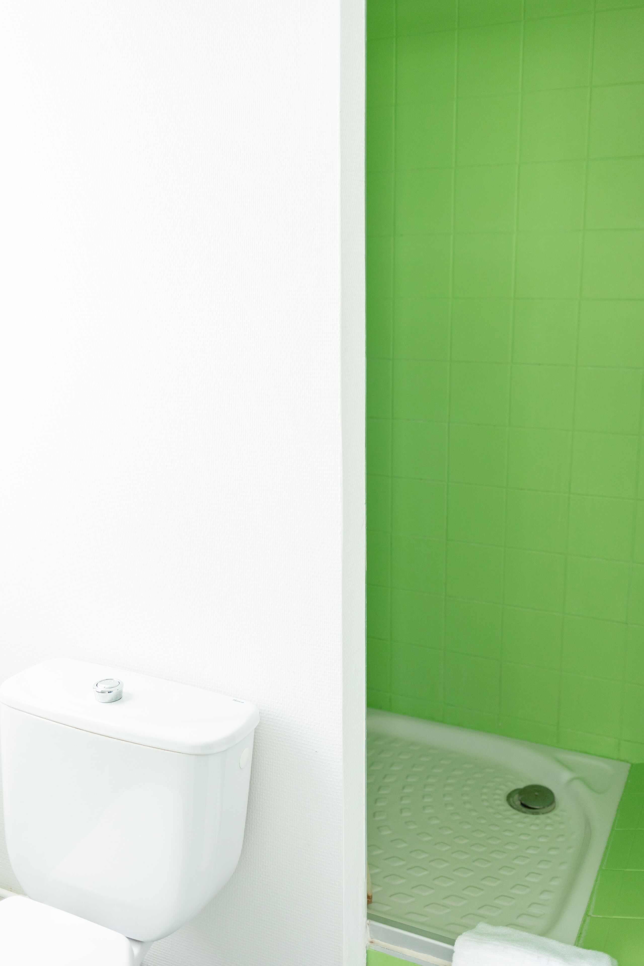 Un baño con inodoro blanco y zona de ducha con azulejos verdes.