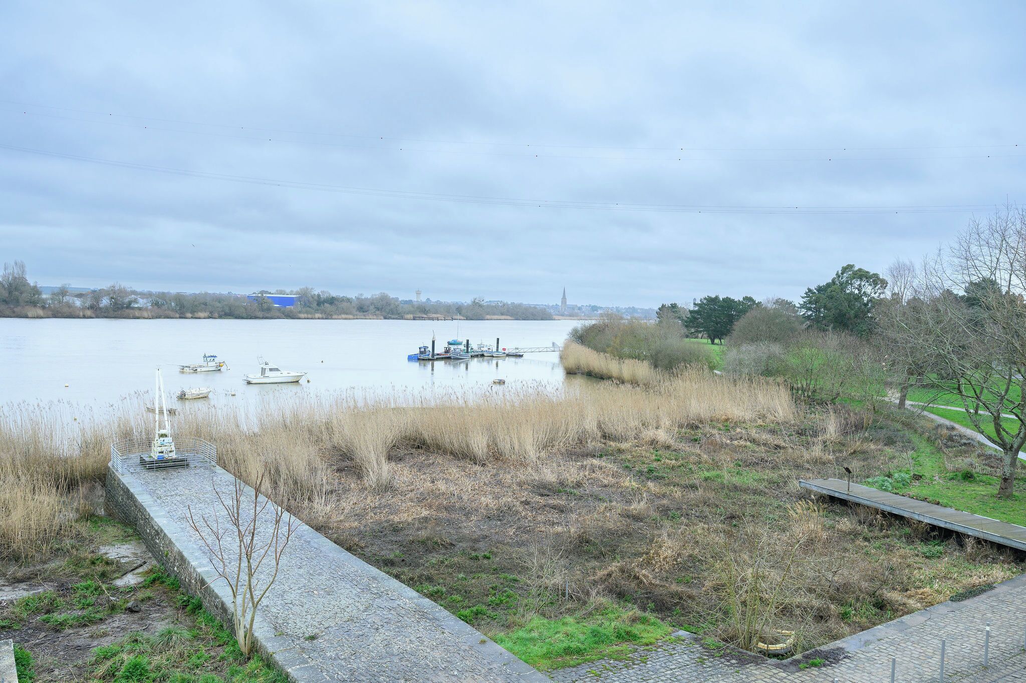 A calm lake with boats, a grassy area, and a distant tower.