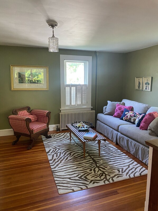 A room with a zebra-patterned rug, a wooden chair, a sofa with colorful pillows, a radiator, and framed pictures on the walls. - Stockbridge Village Cottage With Mountain View’s and walk to town (Stockbridge)
